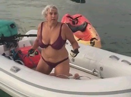 Starsza pani pokazuje, jak się dostać na ponton będąc w wodzie